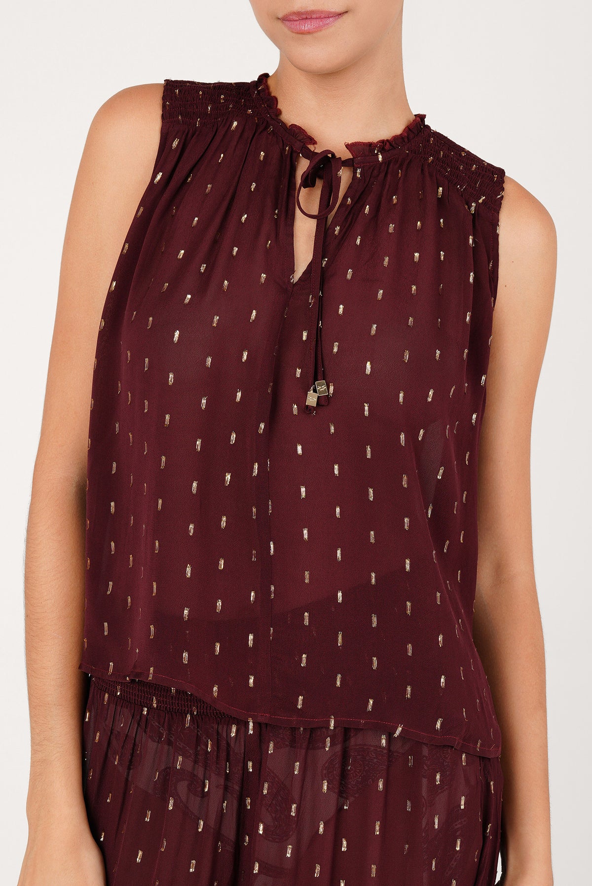 Blusa color vino sin mangas y semitransparente, con trazos dorados y cordón con cuenta al cuello
